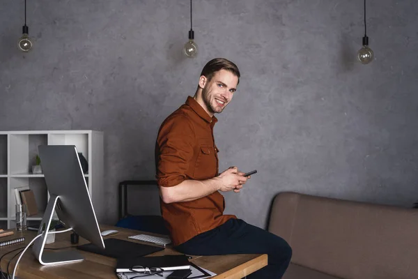 Lachende Jonge Zakenman Gebruikend Smartphone Terwijl Buurt Van Werkplek — Stockfoto