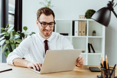 yakışıklı gülümseyen iş adamı ile smartphone Masadaki laptop ile çalışma
