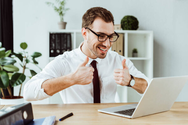 handsome successful businessman making video call on laptop and showing thumbs up