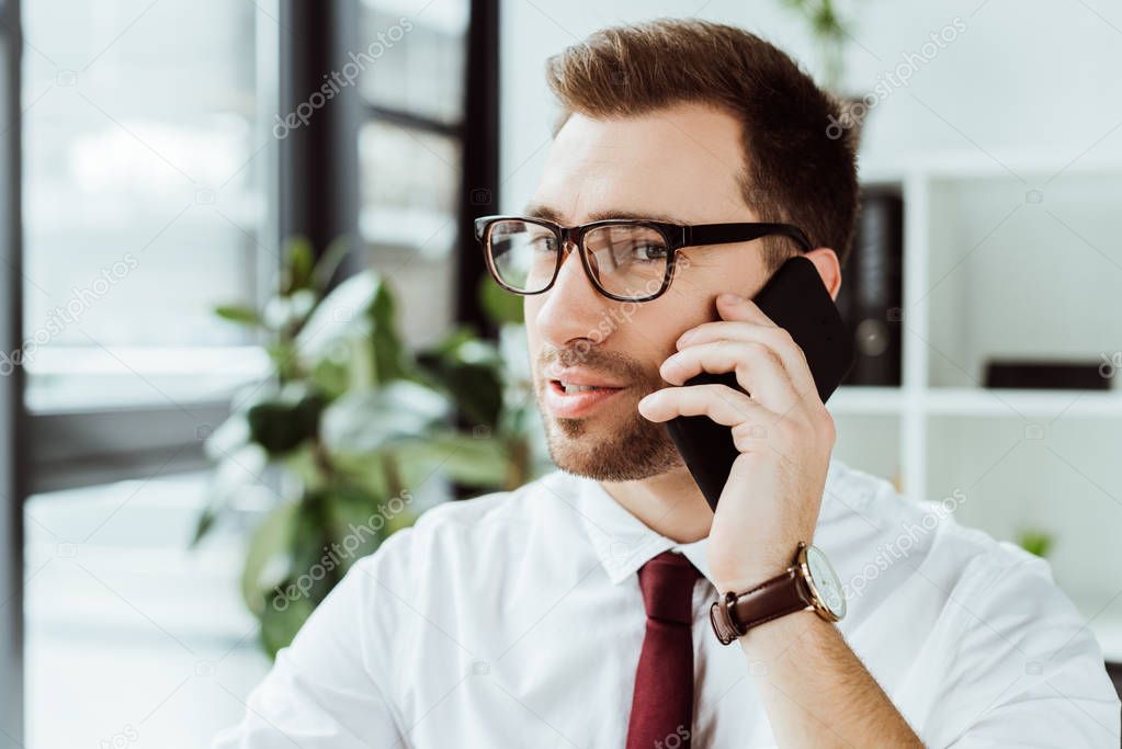 handsome businessman in eyeglasses talking on smartphone in office