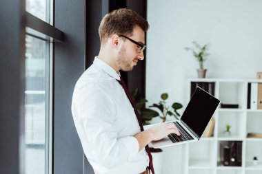 Modern ofiste dizüstü bilgisayar kullanan yakışıklı iş adamı.