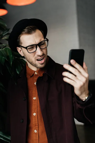 Handsome Stressed Man Hat Glasses Looking Smartphone — Free Stock Photo