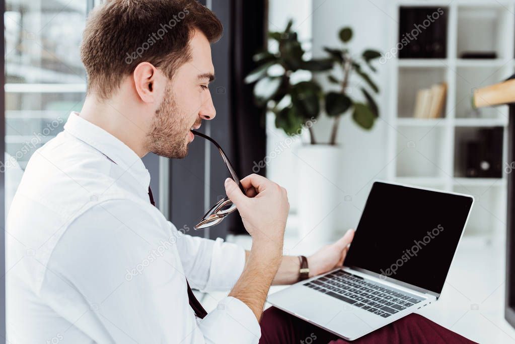 handsome thoughtful businessman with eyeglasses using laptop in office