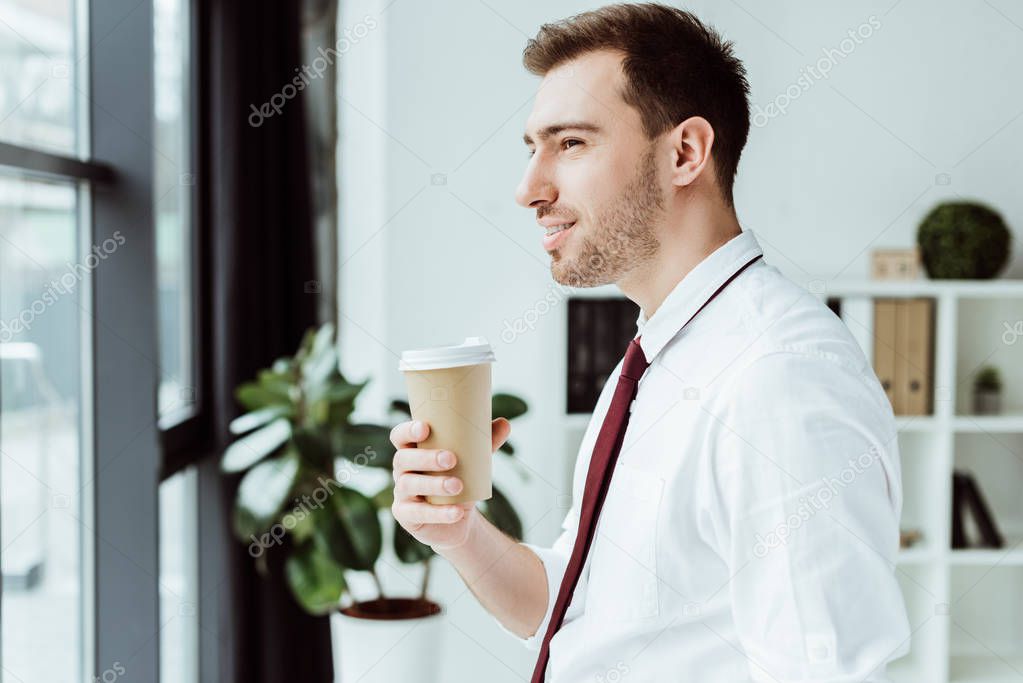 businessman holding disposable cup of coffee and looking at window