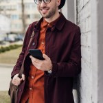 Pohledný módní muž s taškou pomocí smartphonu