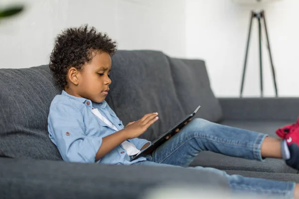 Thoughtful boy using digital tablet on sofa — Stock Photo