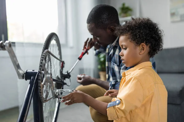 Афро отец и сын ремонтируют велосипед — стоковое фото