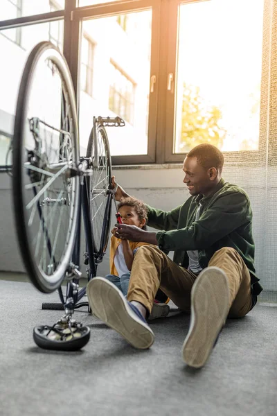 Afro padre e hijo reparando bicicleta - foto de stock