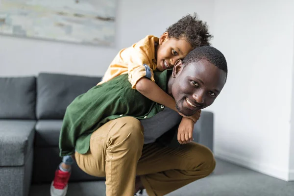 Afro hijo piggybacking en padre en casa - foto de stock