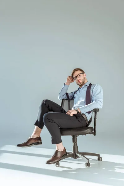 Молодой расслабленный бизнесмен сидит на стуле на светлом фоне стены — стоковое фото