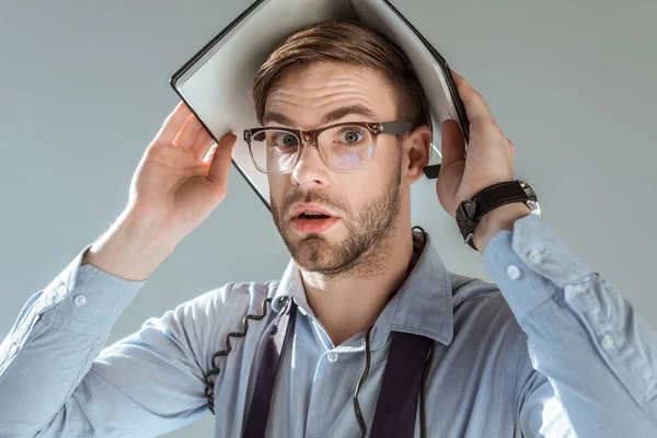 Confused businessman holding notebook on his head isolated on grey — Stock Photo