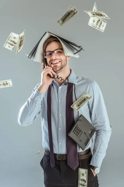 Dollar bills falling on businessman holding notebook on his head while talking on phone isolated on grey — Stock Photo