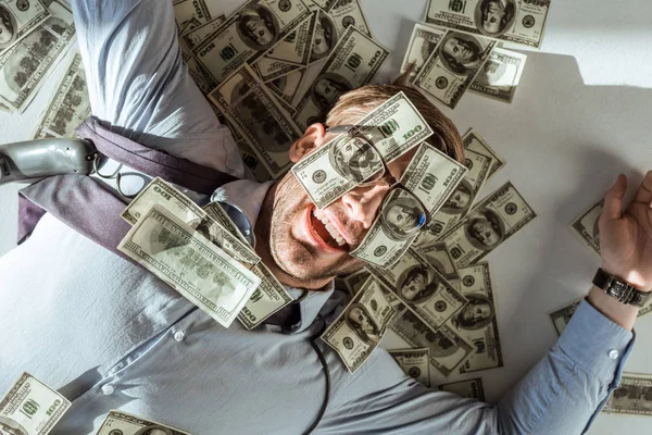 Young happy rich businessman lying on floor with dollar bills covering his face — Stock Photo