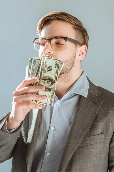 Молодой бизнесмен целует долларовые купюры изолированные на сером — стоковое фото