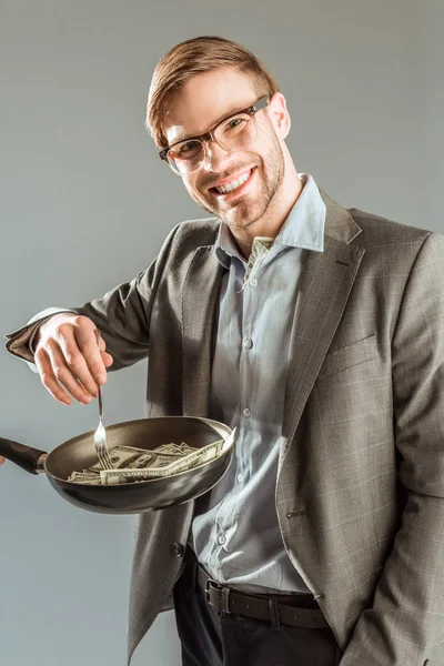 Jovem empresário fritando notas de dólar em pan isolado em cinza — Fotografia de Stock