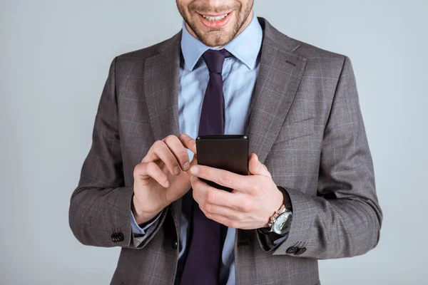 Selbstbewusster Geschäftsmann nutzt Smartphone isoliert auf grau — Stockfoto