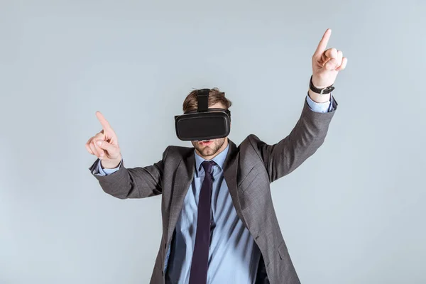 Young businessman in vr headset pointing up isolated on grey — Stock Photo