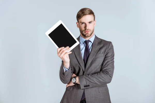 Молодой вдумчивый бизнесмен держит цифровой планшет изолированный на сером — стоковое фото