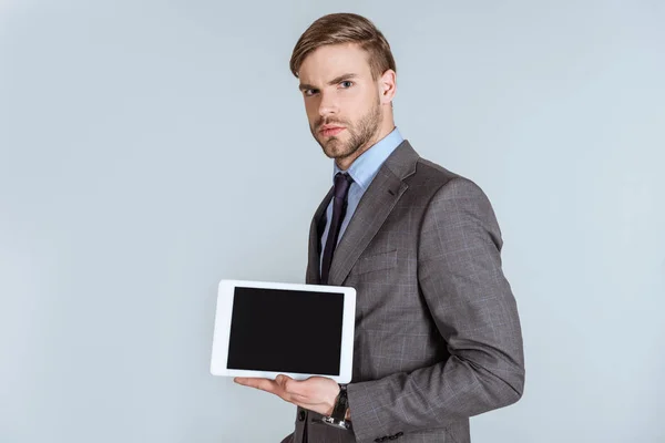 Joven empresario reflexivo que presenta tableta digital aislada en gris - foto de stock
