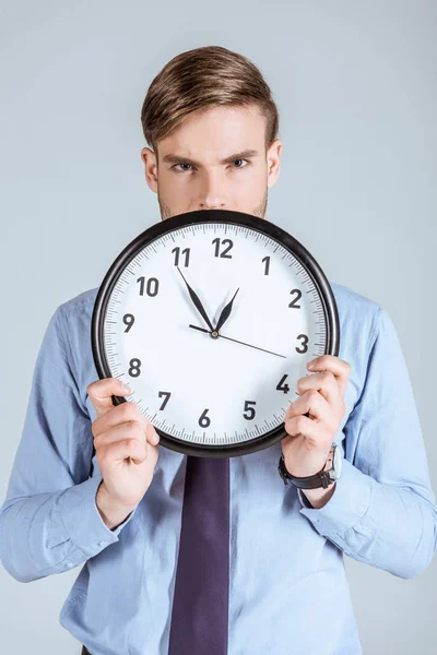 Businessman in shirt holding clock in front of him isolated on grey — Stock Photo