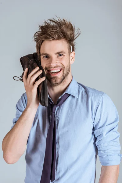 Empresario sobrecargado de trabajo con el pelo desordenado usando zapato como teléfono aislado en gris - foto de stock