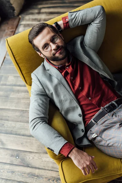 Vista aérea de homem sorridente elegante em terno sentado no sofá — Fotografia de Stock