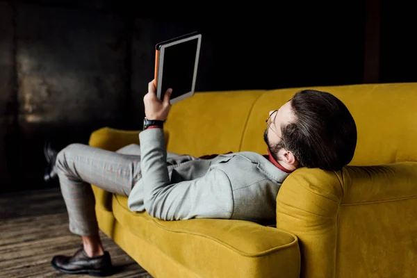 Man using digital tablet while lying on couch — Stock Photo