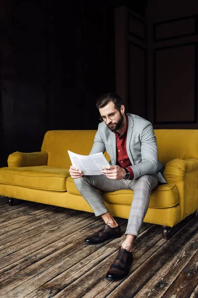 Стильний чоловік у костюмі читає газету і сидить на жовтому дивані — стокове фото
