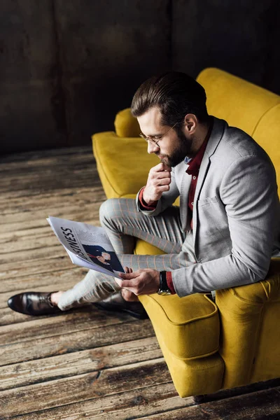 Hombre pensativo elegante leyendo periódico de negocios y sentado en el sofá - foto de stock