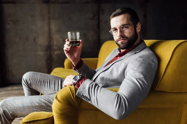 Elegante hombre guapo sosteniendo vaso de whisky y mirando a la cámara - foto de stock