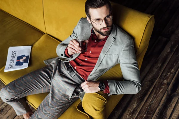 Eleganter Mann mit einem Glas Whiskey auf dem Sofa mit Zeitung — Stockfoto