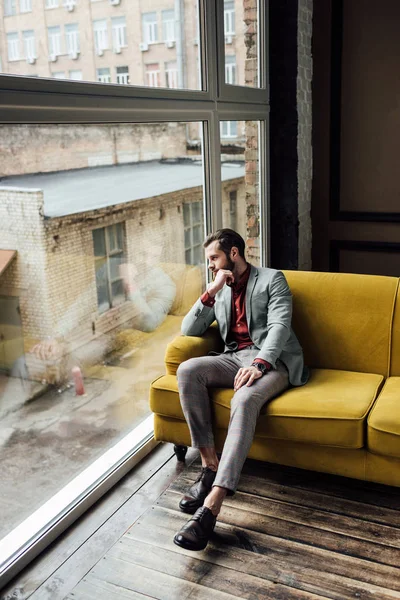 Стильний вдумливий чоловік сидить на жовтому дивані і дивиться на вікно — Stock Photo