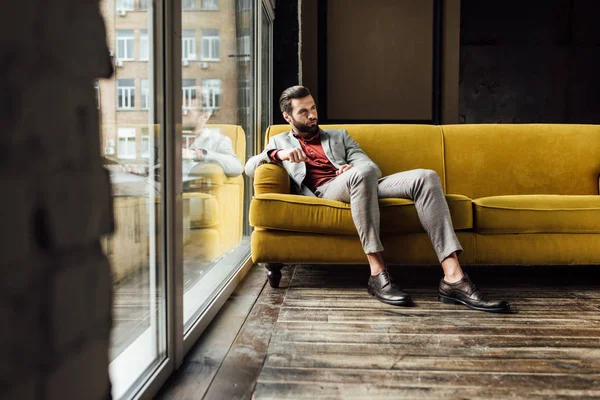 Homme à la mode assis sur un canapé jaune à la grande fenêtre — Photo de stock