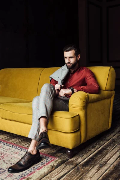 Élégant bel homme assis sur un canapé jaune — Photo de stock