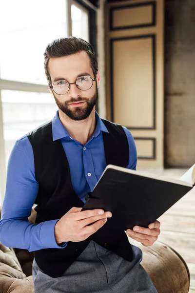 Fashionable elegant businessman in eyeglasses holding notebook in loft interior — Stock Photo