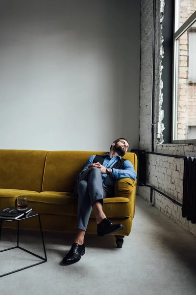 Eleganter Mann ruht auf gelbem Sofa mit Alkoholgetränk auf Tisch in der Nähe — Stockfoto