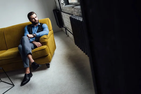 Stylish handsome man sitting on yellow couch in loft — Stock Photo