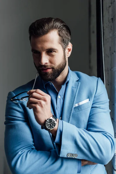 Handsome man bearded in blue trendy suit holding glasses — Stock Photo