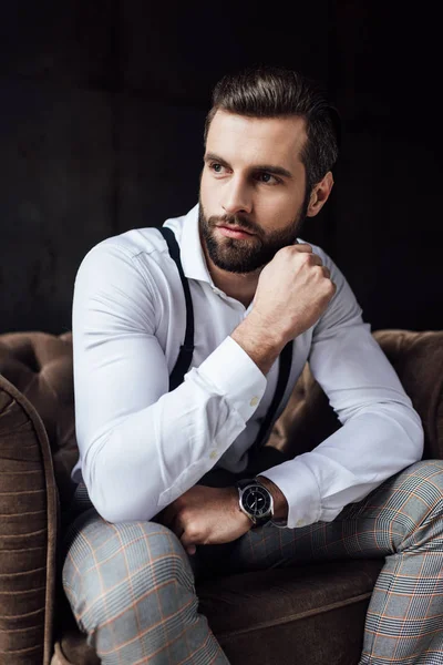 Stylish man in suspenders thinking and sitting in armchair — Stock Photo