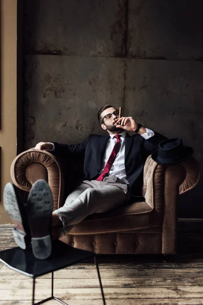 Fashionable businessman sitting in armchair and smoking cigar — Stock Photo