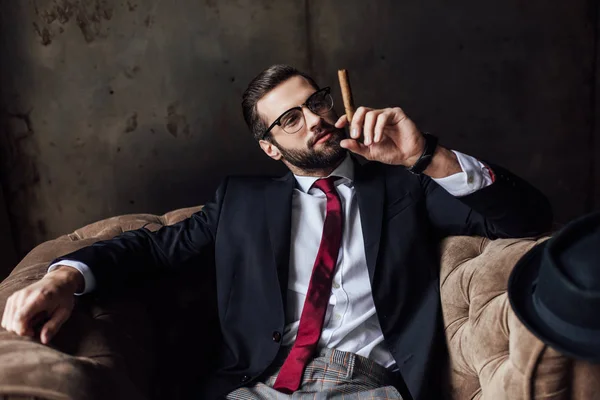 Модний чоловік сидить у кріслі і тримає сигару — стокове фото
