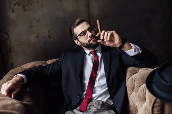 Homem elegante sentado em poltrona e segurando charuto — Fotografia de Stock