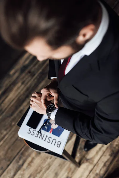 Vista aerea di uomo d'affari guardando orologio da polso mentre in piedi a sgabello con giornale aziendale e smartphone — Foto stock