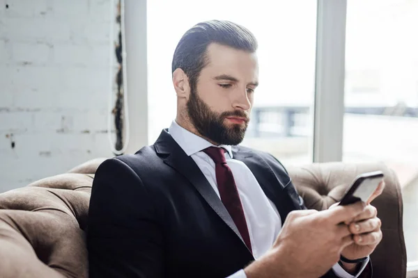Homem de negócios barbudo mensagens no smartphone e sentado em poltrona — Fotografia de Stock