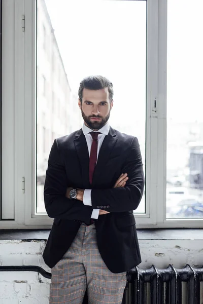 Handsome serious businessman posing with crossed arms at window — Stock Photo
