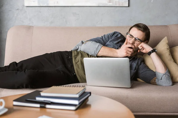 Erschöpfter gähnender Mann arbeitet mit Laptop auf Couch — Stockfoto