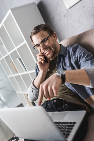 Angry young man talking by phone and pointing at laptop — Stock Photo