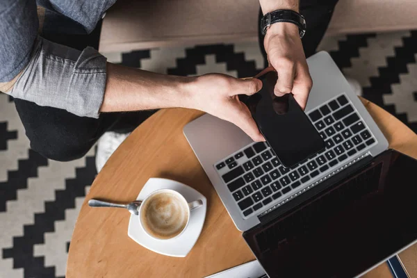 Recadré coup fo homme en utilisant smartphone avec ordinateur portable sur la table basse — Photo de stock