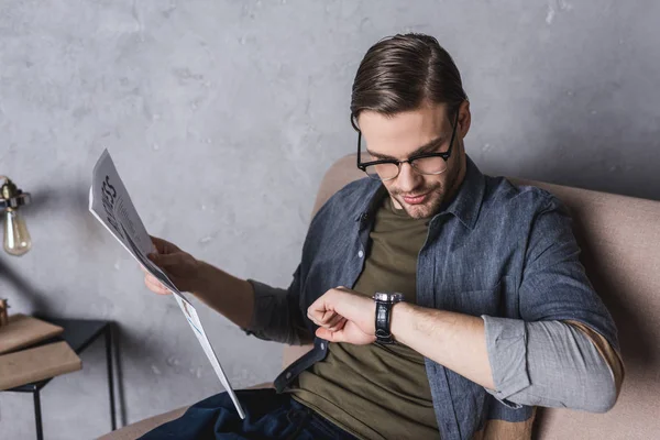 Young businessman with newspaper checking time on his watch — Stock Photo