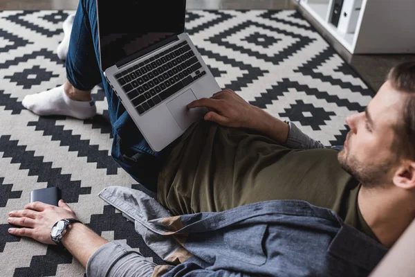 Entspannter junger Mann arbeitet mit Laptop während er auf dem Boden sitzt — Stockfoto